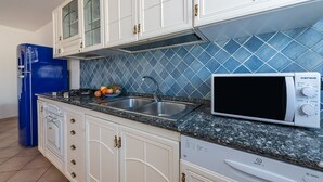 A kitchen with white cabinets, a blue refrigerator, a microwave, and a sink with a blue tiled backsplash. - Casa Tortora (Siniscola)