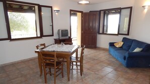 A dining area with a wooden table and chairs, a blue sofa, and a television on a wooden cabinet. - Casa Pompia 3 (Siniscola)