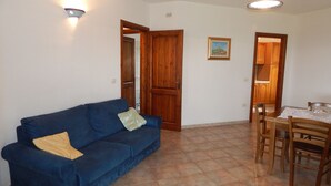 A living room with a blue sofa, a dining table with chairs, and wooden doors. - Casa Pompia 3 (Siniscola)