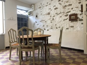 A dining area with a wooden table and four chairs, a checkered floor, a stone wall, and a window. - The P'tit Relais du Canal (Trèbes)