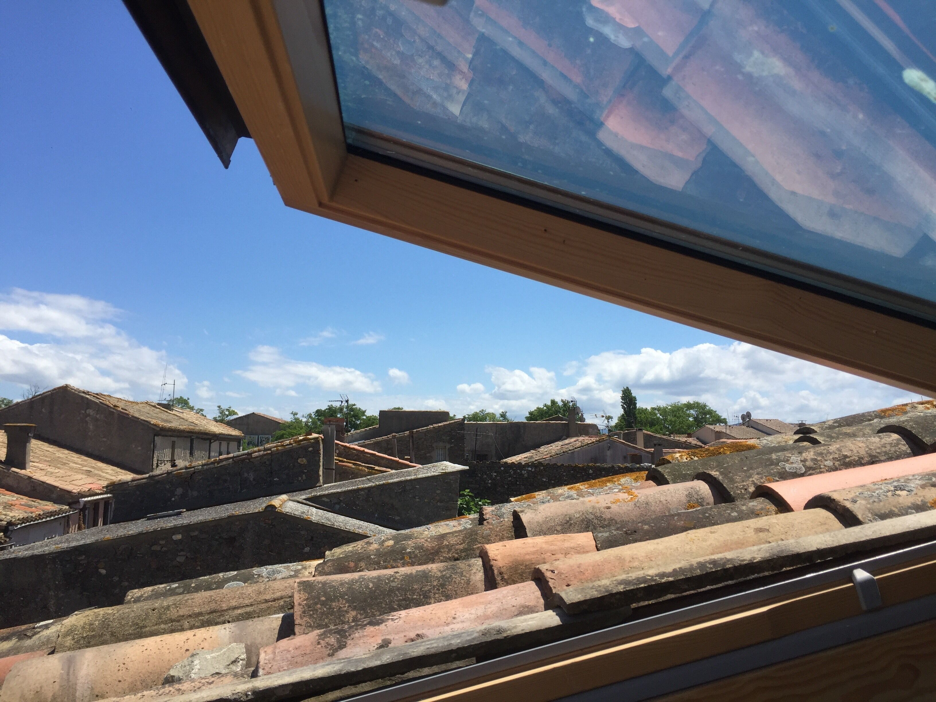 Blick durch ein Fenster auf ein Gebäude mit mehreren Terrassendächern und blauem Himmel.