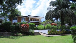 A modern two-story house with a balcony, surrounded by a well-maintained garden with various plants and a lawn. - Rocy Hotel (Mbale)