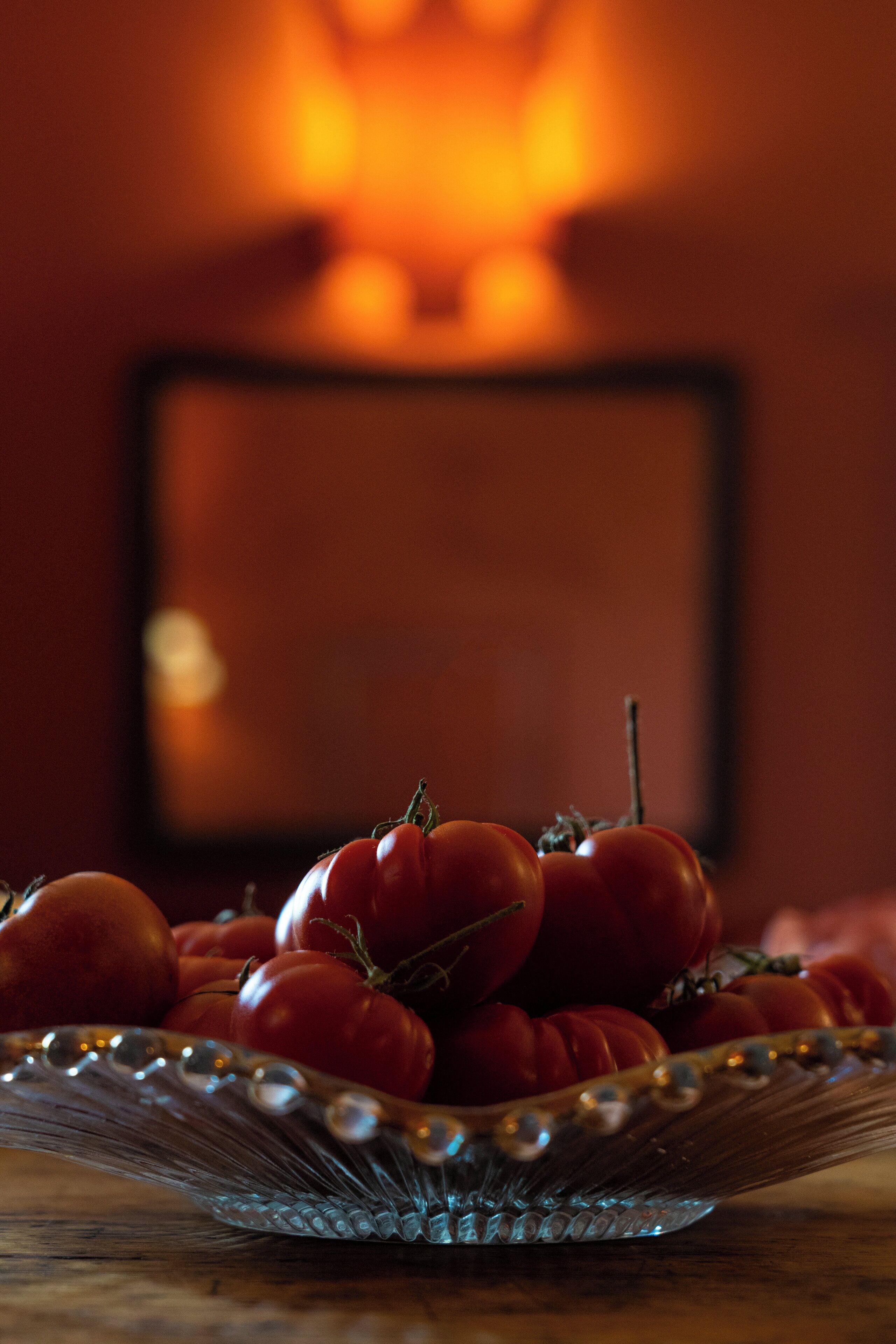 A glass bowl filled with tomatoes on a wooden surface.