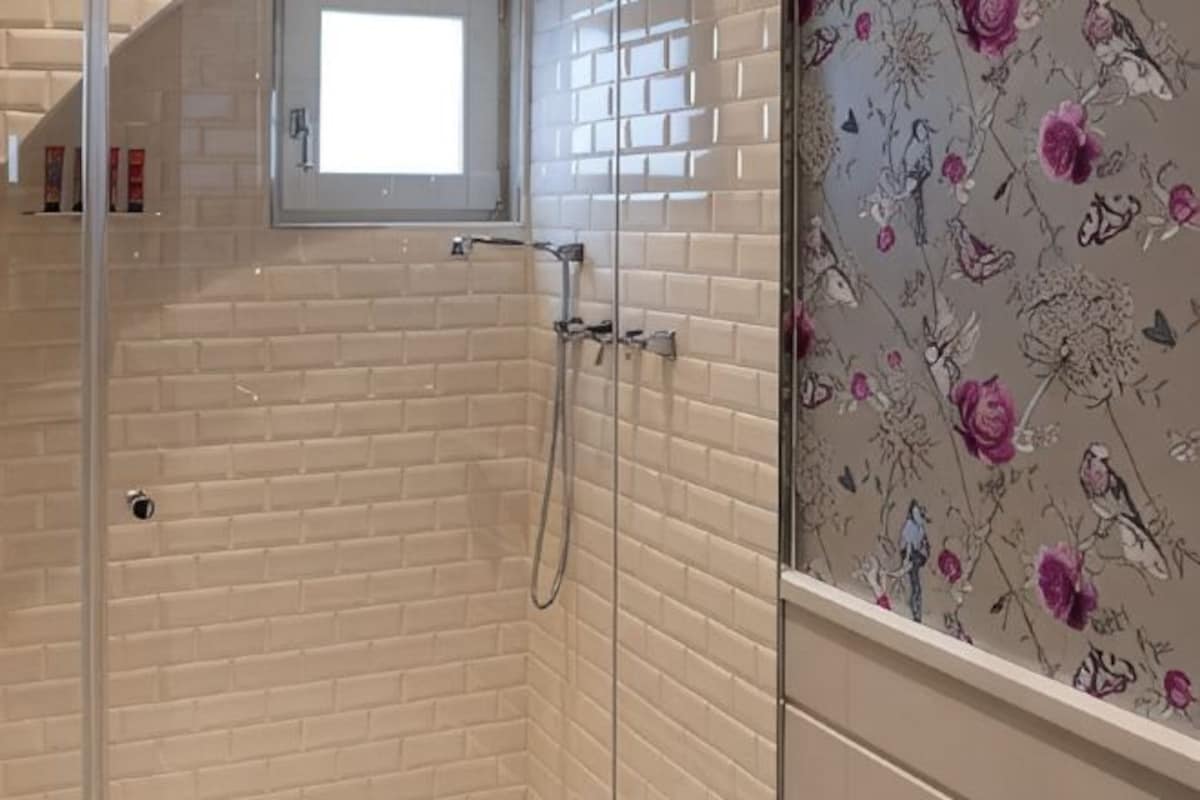 Ducha con mampara de vidrio, una ventana pequeña y pared de azulejos con diseño floral.