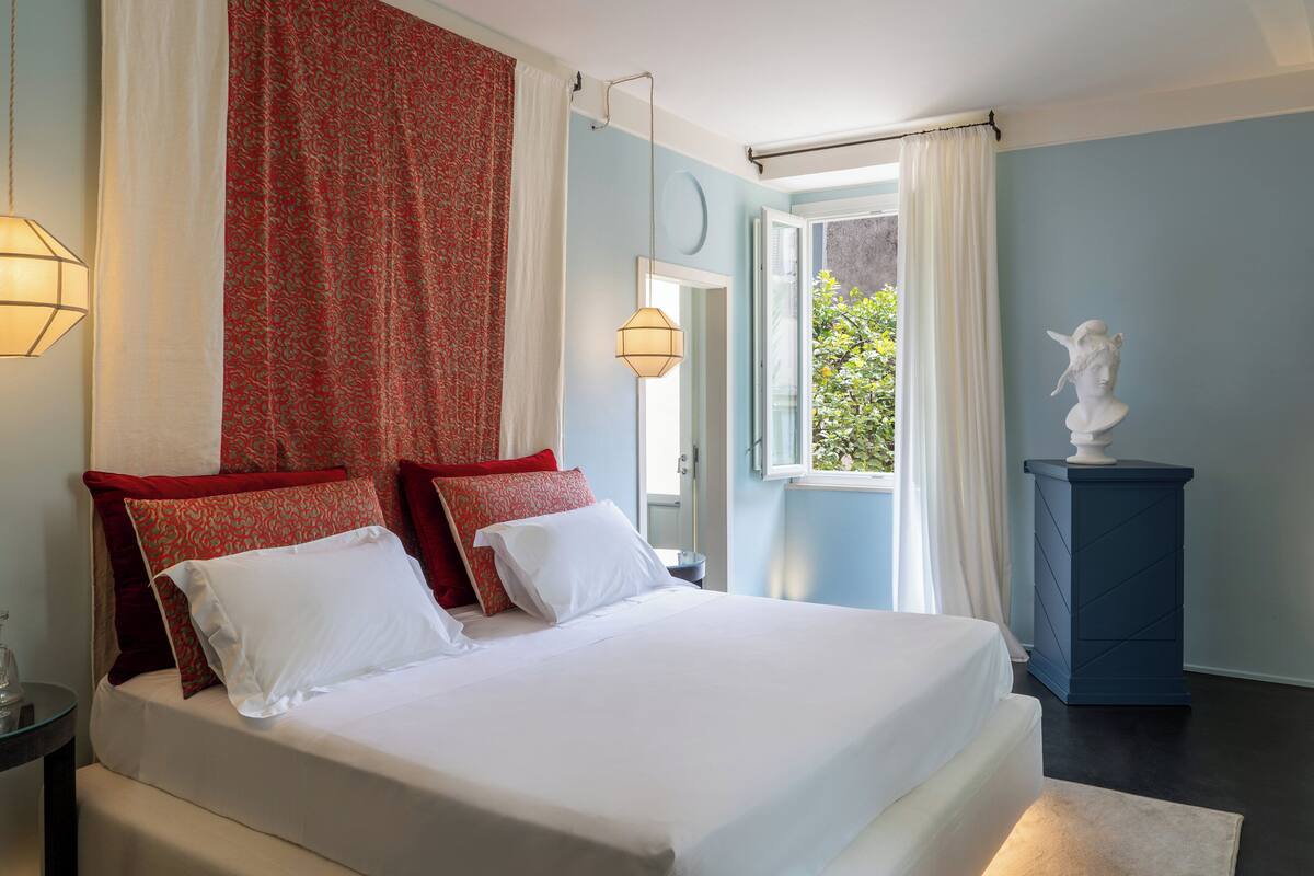 A bedroom with a large bed, a nightstand, a statue, and a window with curtains.
