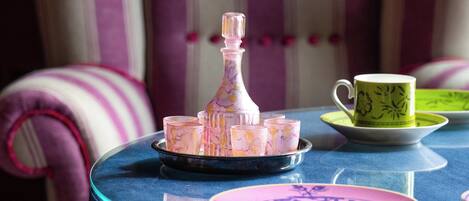 Una mesa redonda con mantel azul, una silla a rayas y una bandeja con una botella, vasos y platos.