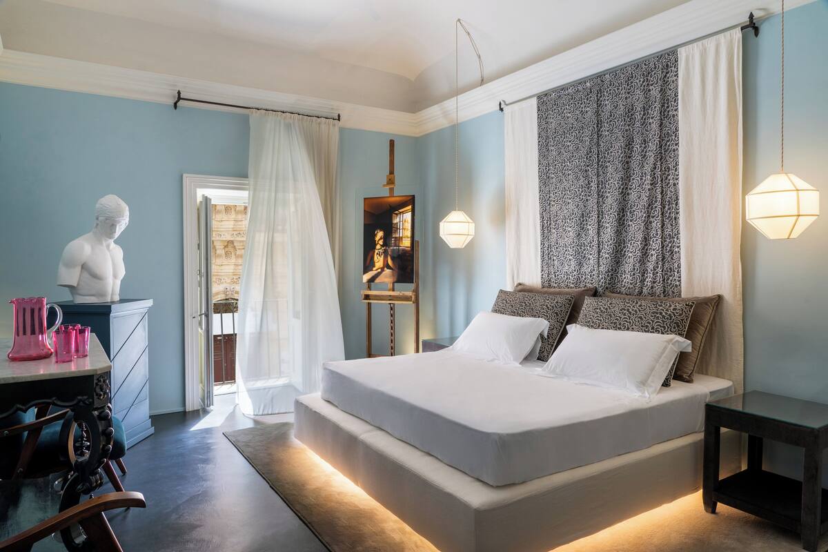 A bedroom with a bed, bedside tables, a dresser, a sculpture, and a patterned tapestry.