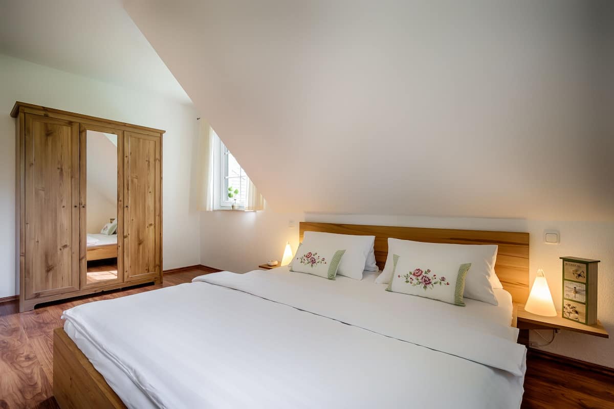A bedroom with a large bed, wooden wardrobe, and a nightstand with a lamp.