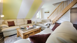 A modern living room with a high ceiling, a wooden staircase, and a large window providing natural light.