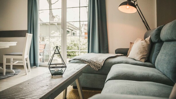 A cozy living room with a sofa, a table with a lantern, and a view through a glass door.