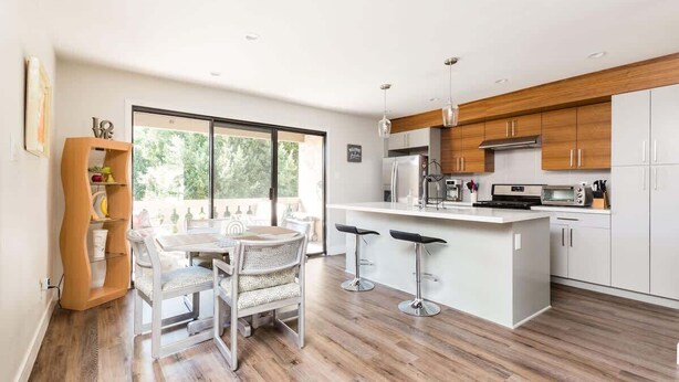 A modern kitchen with white cabinets, a central island with bar stools, and a dining area with a table and chairs.