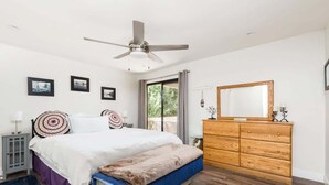 A bedroom with a bed, a wooden dresser, a ceiling fan, and framed pictures on the wall.
