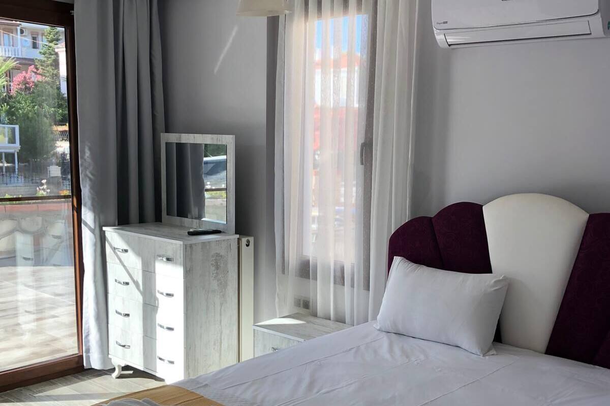 A hotel room with a bed, a desk with a television, an air conditioning unit, and a view of the outside.
