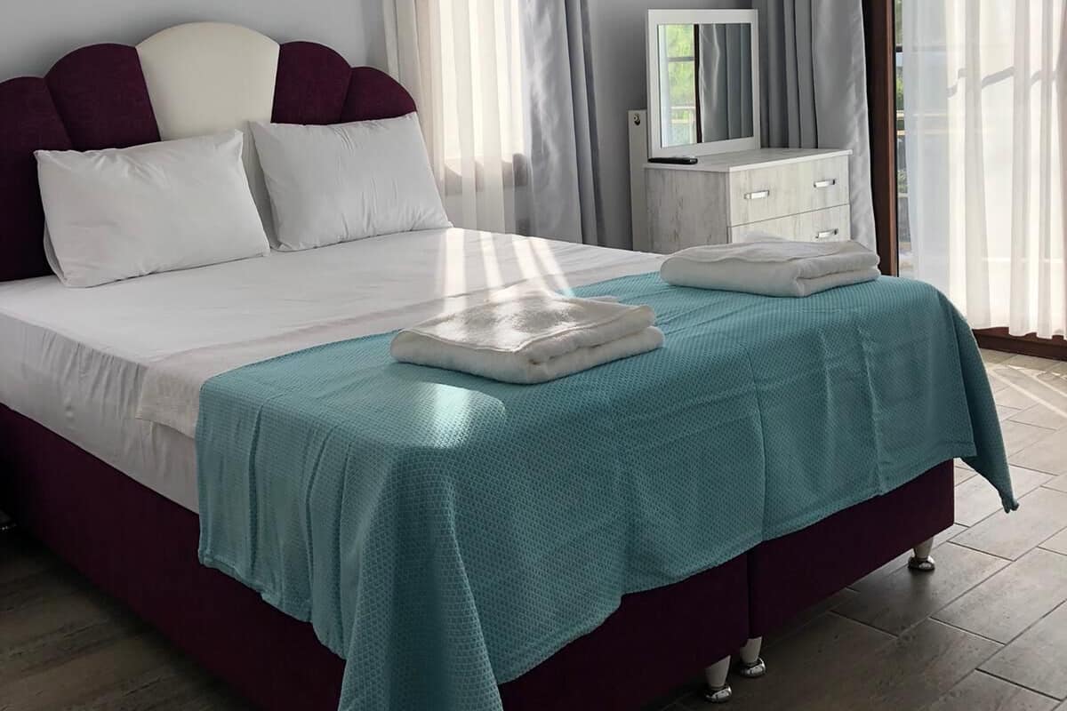 A neatly arranged bedroom with a bed, a bedside table, a television, and a window with curtains.