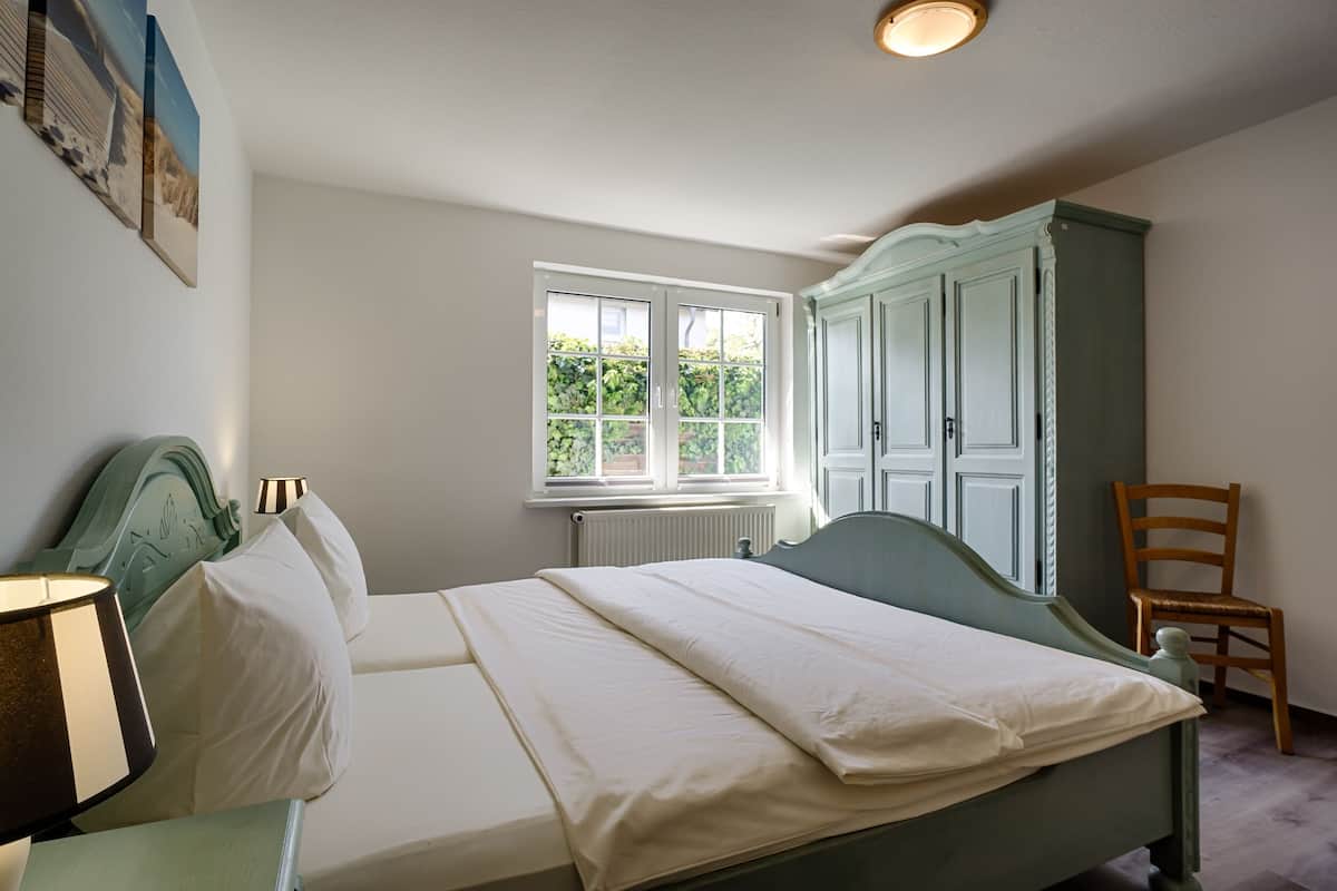 A bedroom with a bed, a window, a chair, and a wardrobe.