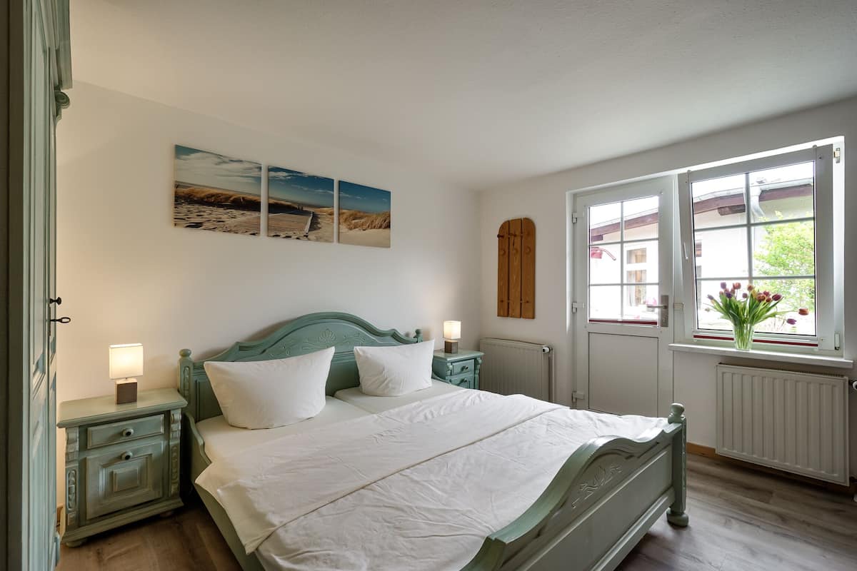 A bedroom with a bed, nightstands, a window with a view, and a wall-mounted artwork.