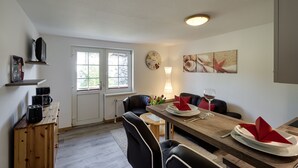 Ein Essbereich mit einem Holztisch, schwarzen Stühlen, einer Uhr, einer Lampe und einem Fenster mit Blick auf Bäume.