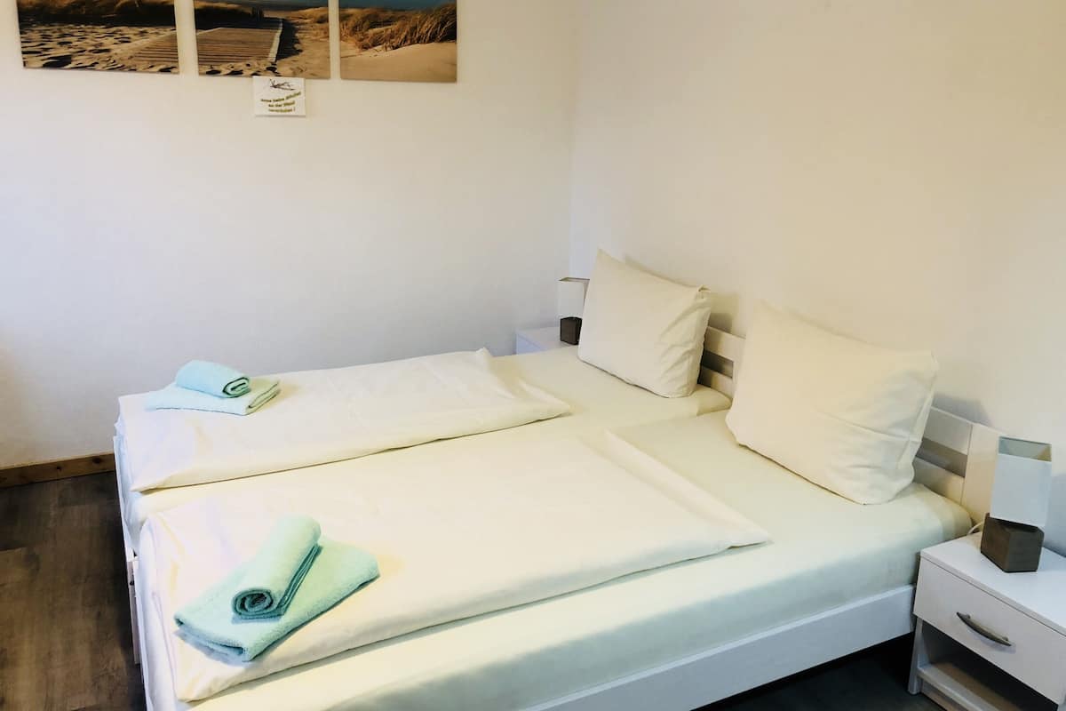 A neatly made bed with white linens and a blue towel, a bedside table with a lamp, and a wall with three framed pictures.