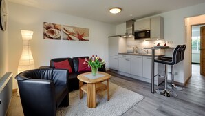 Ein modernes Wohnzimmer mit einer Couch, einem Couchtisch und einer Küchenzeile mit Mikrowelle und Schränken.