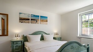 Ein Schlafzimmer mit einem Bett, zwei Nachttischen und einem Fenster mit Blick auf Grünfläche.