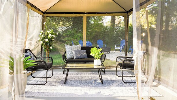 Un espace extérieur aménagé, abrité, avec un canapé, deux fauteuils et une table.