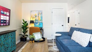 Un salon avec un canapé bleu, un meuble turquoise, une télévision, un tableau et une porte.