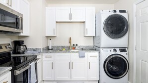Une cuisine compacte avec des meubles blancs, un four à micro-ondes encastré, une machine à café et un lave-linge à chargement frontal.
