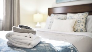 Un lit bien fait, recouvert d’une couvre-lit à motifs bleus et blancs, avec une pile de serviettes pliées et une tête de lit en bois.