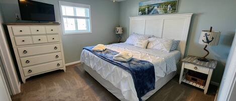 A bedroom with a bed, dresser, nightstand, lamp, and a painting on the wall.