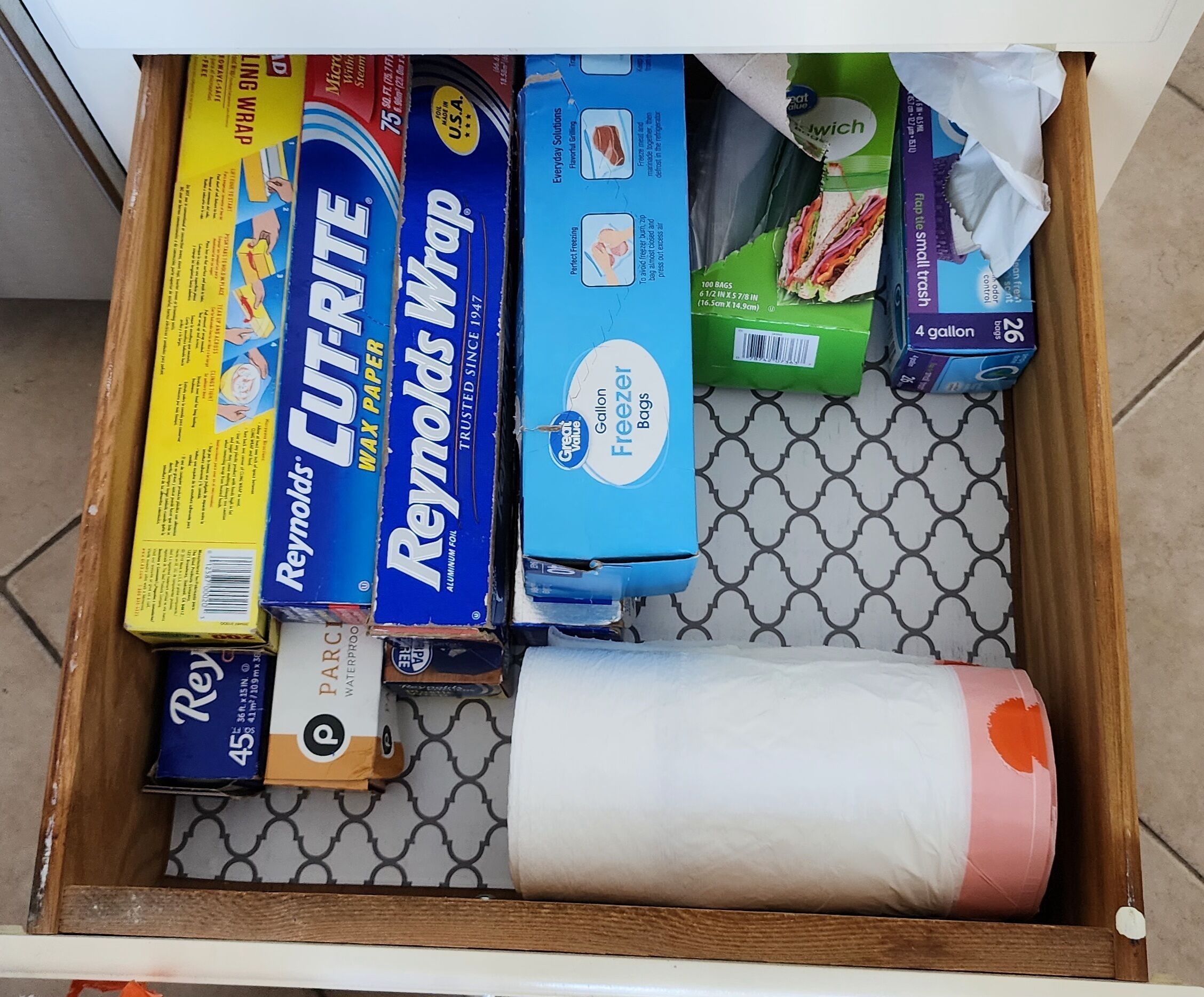 A drawer containing various household items including paper towels, aluminum foil, and a roll of toilet paper.