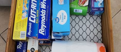 A drawer containing various household items including paper towels, aluminum foil, and a roll of toilet paper.