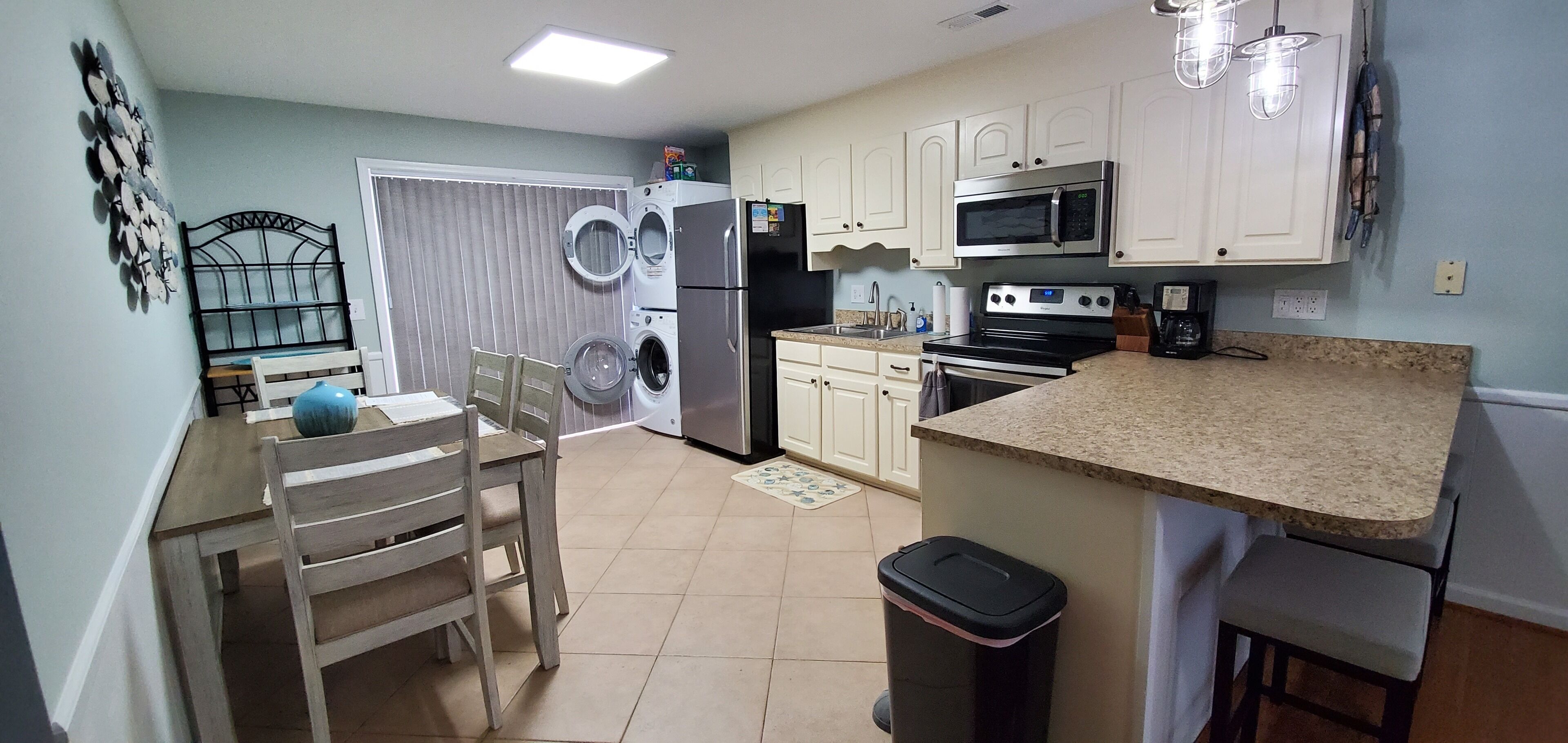 A kitchen with a washing machine, refrigerator, microwave, stove, and a dining area with chairs and a table.