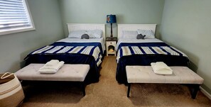 Ein Doppelzimmer mit zwei Betten, jeweils mit passendem Kopfteil und Fußteil, einem Nachttisch mit Lampe und einer Sitzbank am Fußende jedes Bettes.