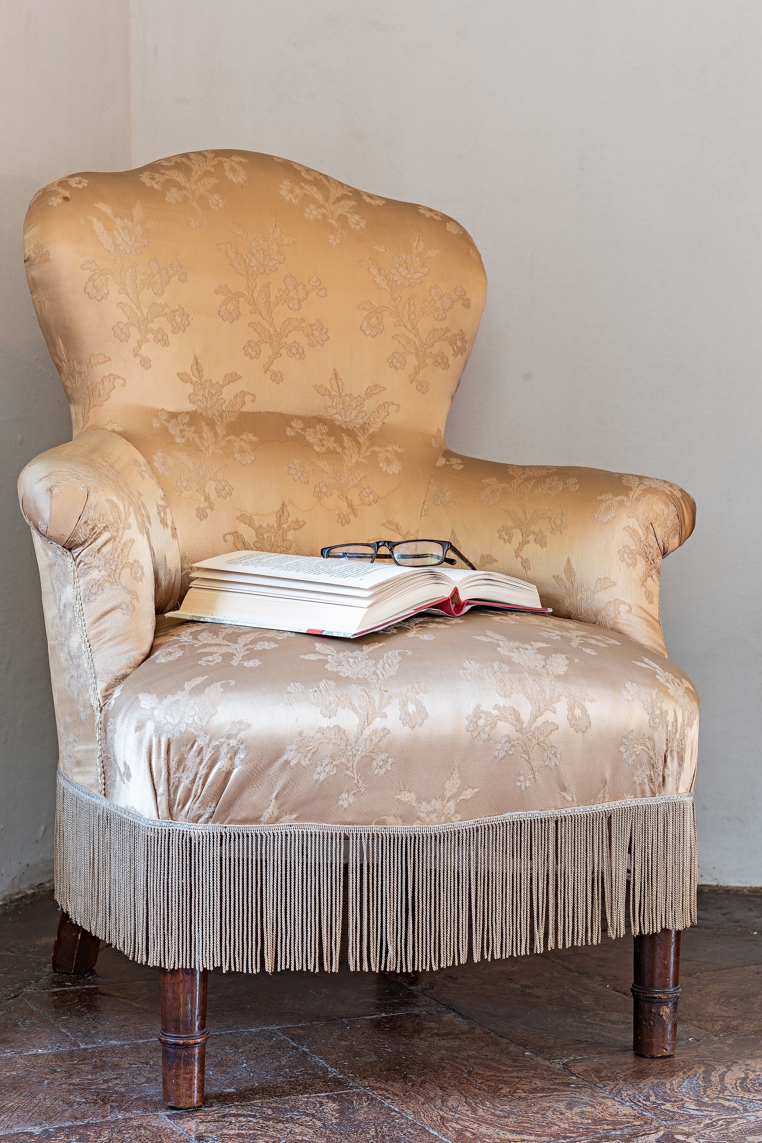 Un fauteuil classique orné d’un motif floral, une paire de lunettes et un livre ouvert posés dessus.