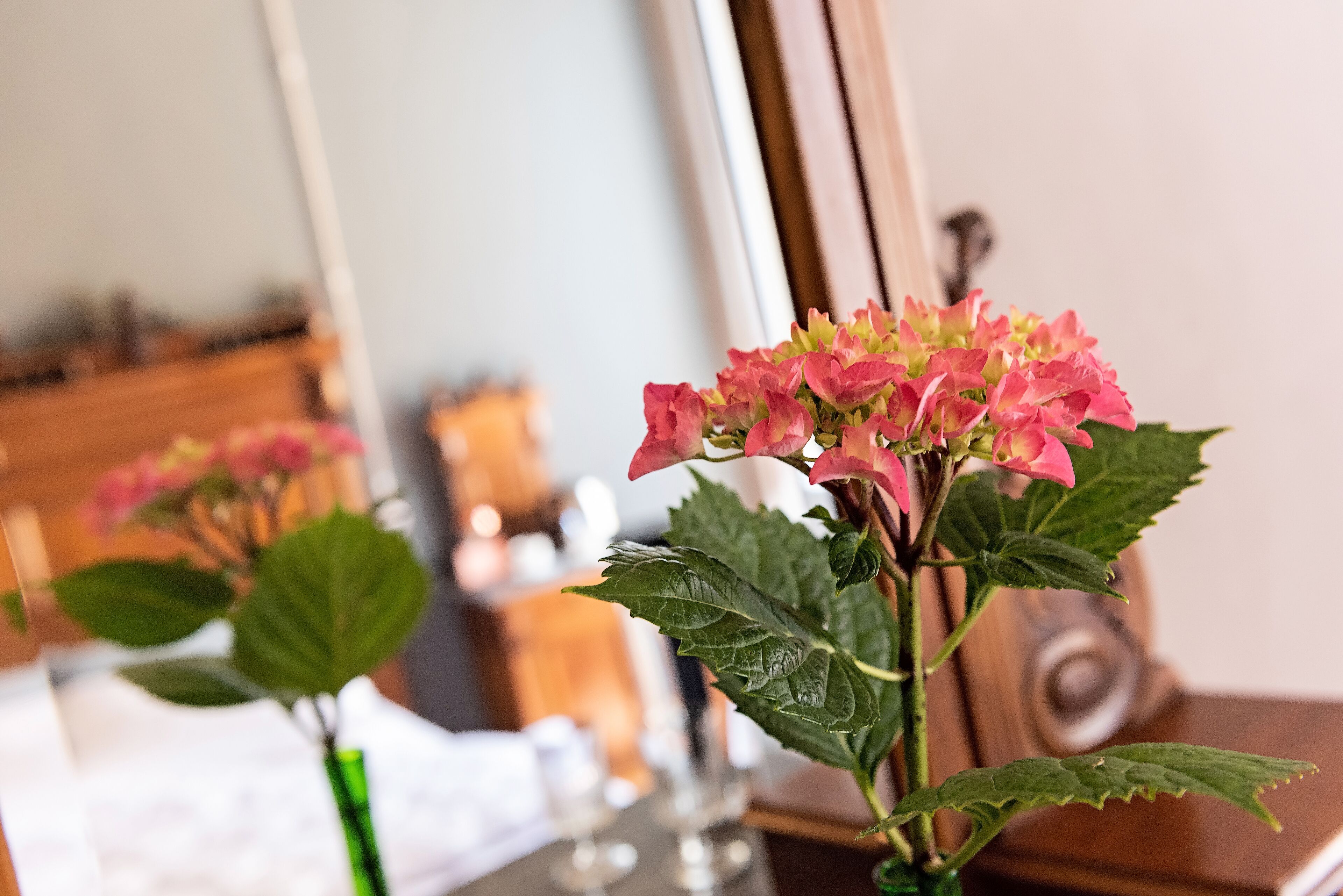 Una habitación con una cama, un tocador y un espejo que refleja un arreglo floral rosa.