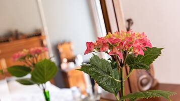 Una habitación con una cama, un tocador y un espejo que refleja un arreglo floral rosa.