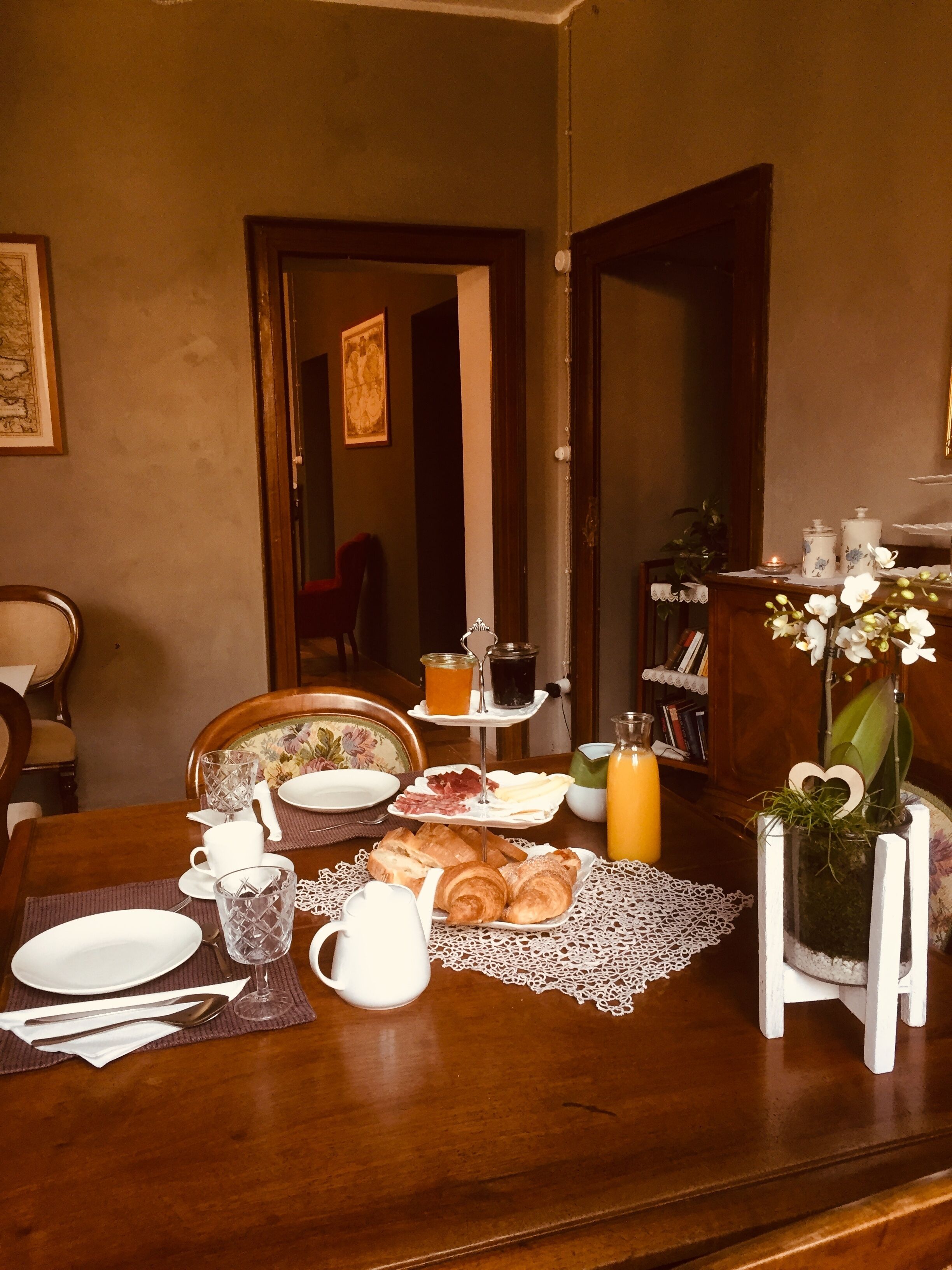 A dining table set with breakfast items, including croissants, a teapot, and a pitcher.