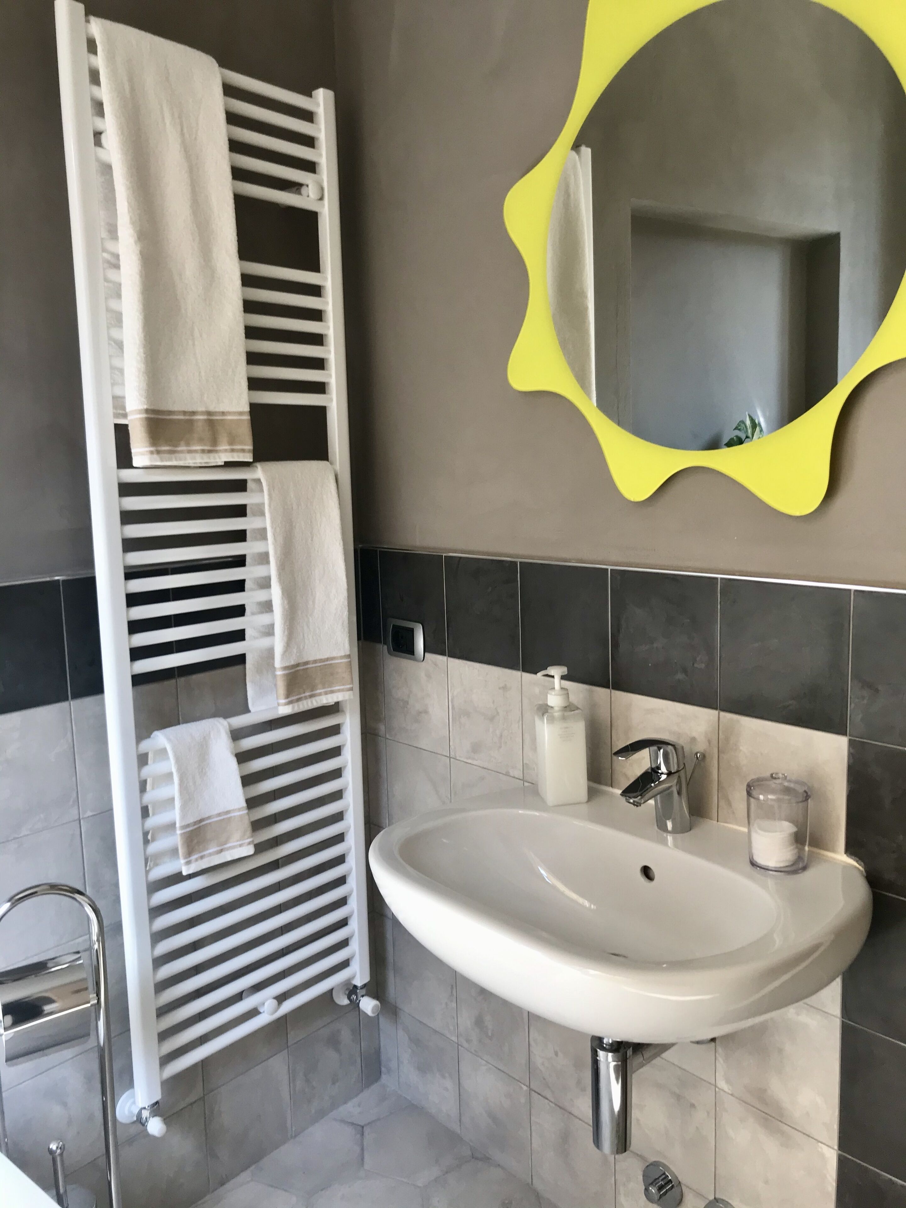 A bathroom with a white towel rack, a sink with a soap dispenser, and a yellow mirror.