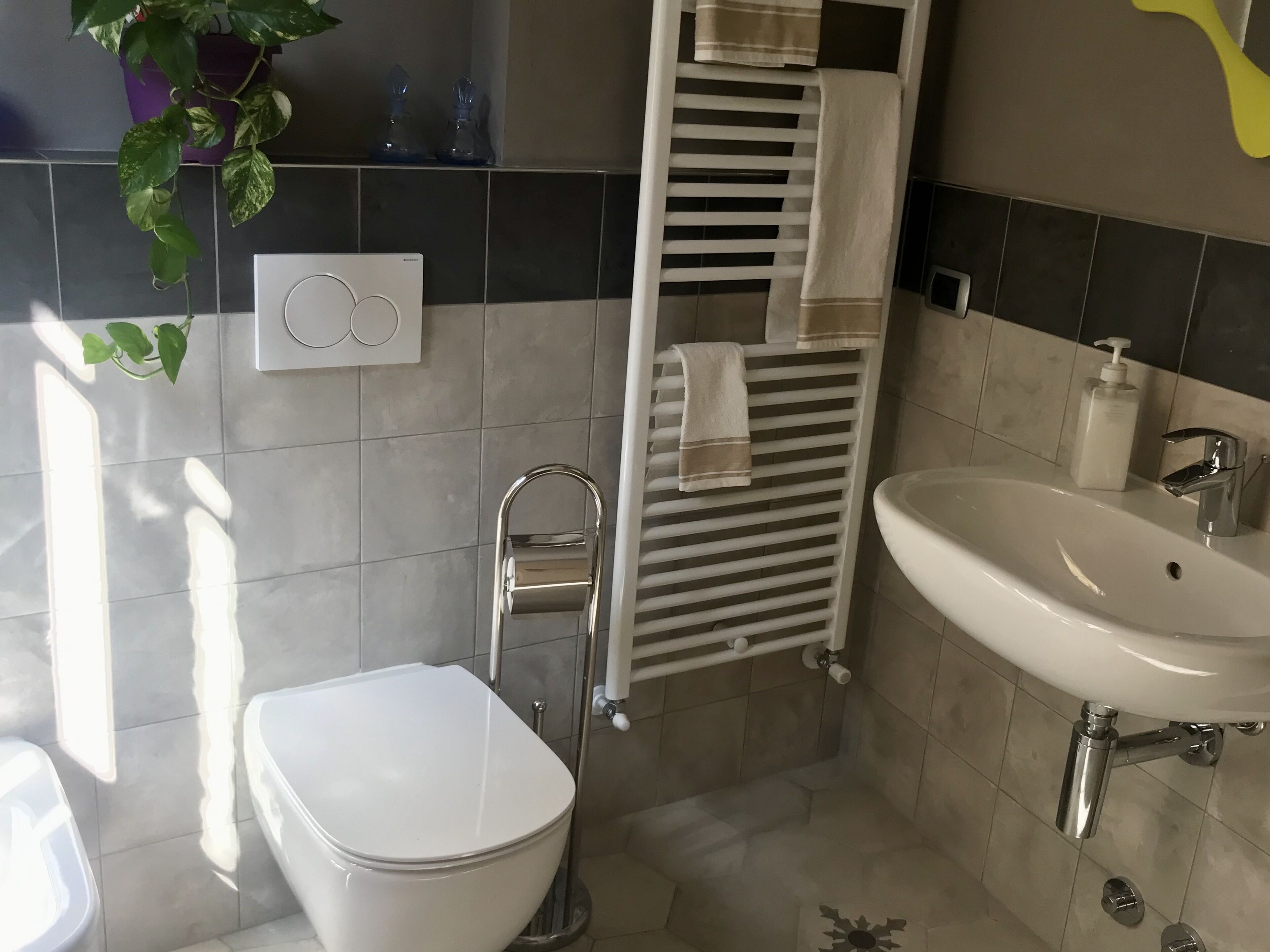 A bathroom with a toilet, sink, towel rack, and a wall-mounted light switch.