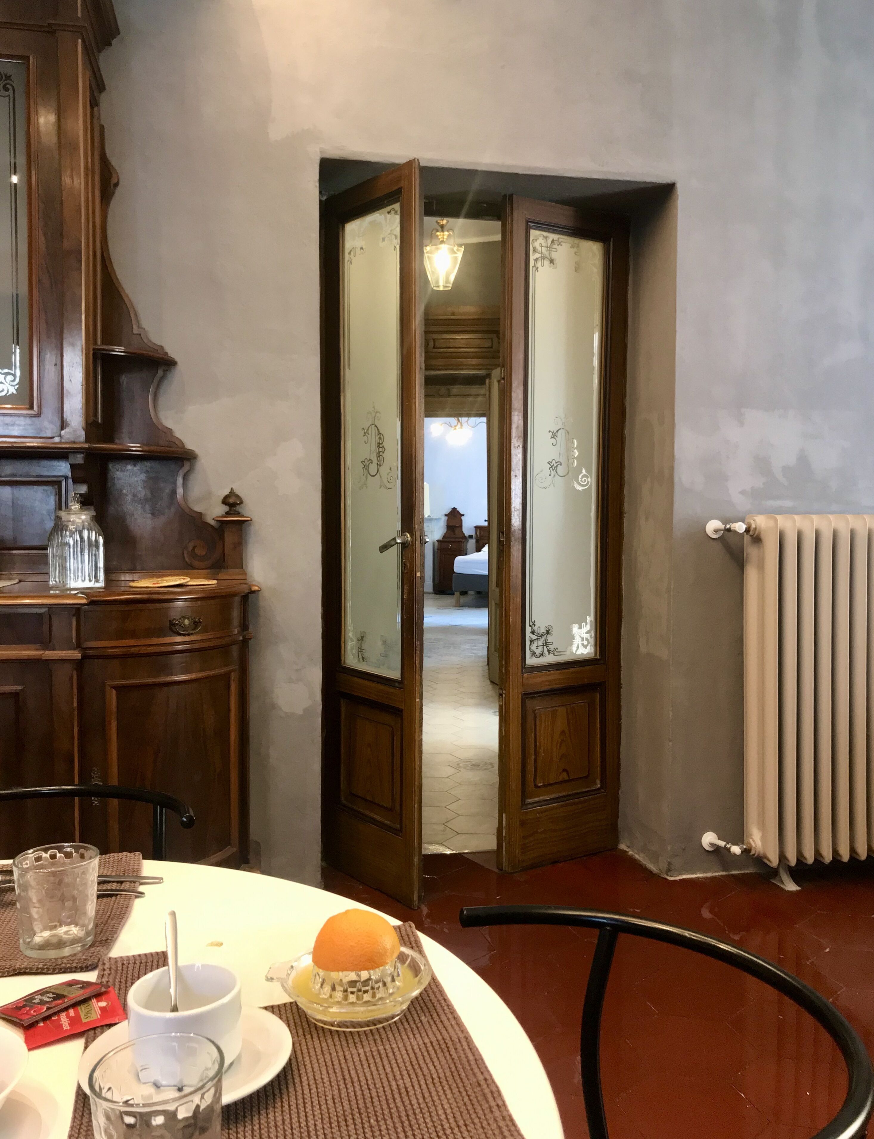 A dining area with a table set for two, a wooden cabinet, and a view into another room through an open door.