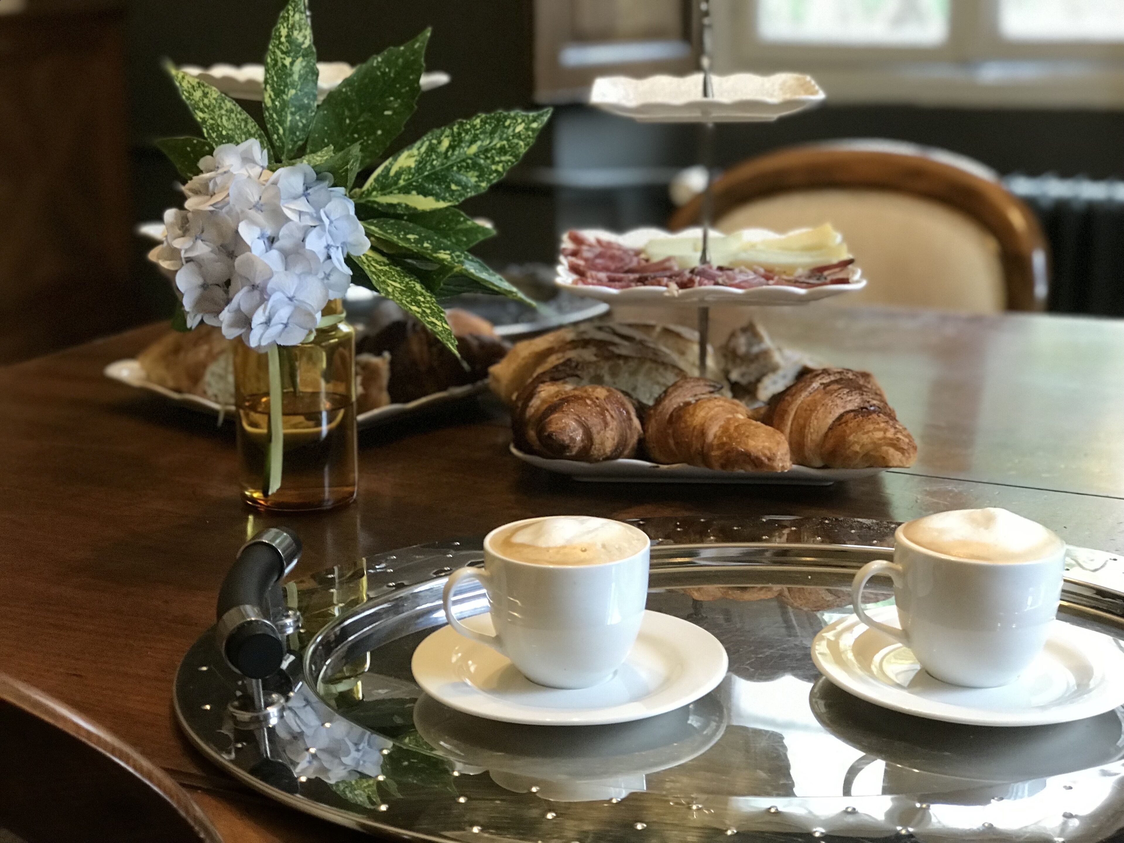 A tray with croissants, a plate of ham, and a vase with flowers on a table.