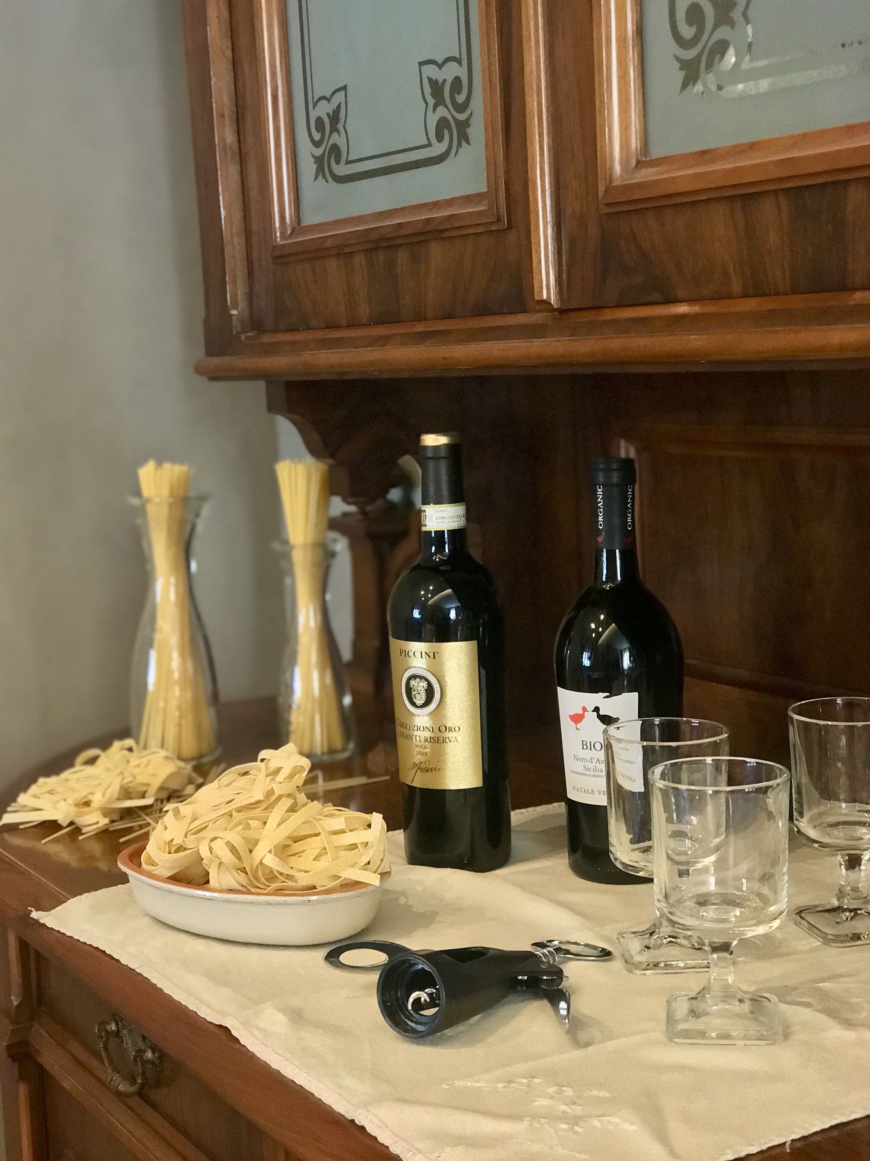 A wooden cabinet with two wine bottles and glasses on a table.