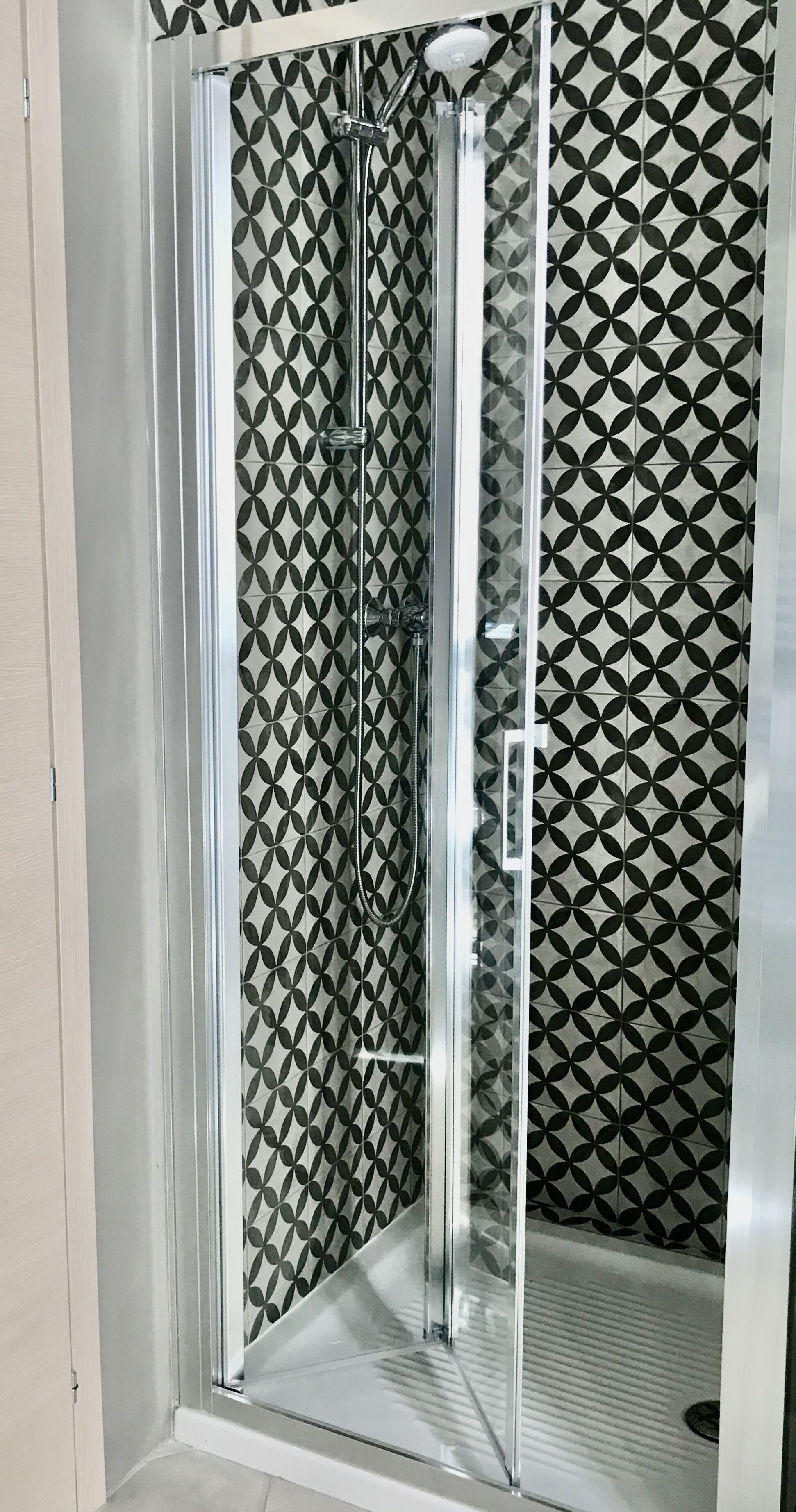 Eine gläserne Dusche mit einem geometrischen Fliesenspiegel an den Wänden.