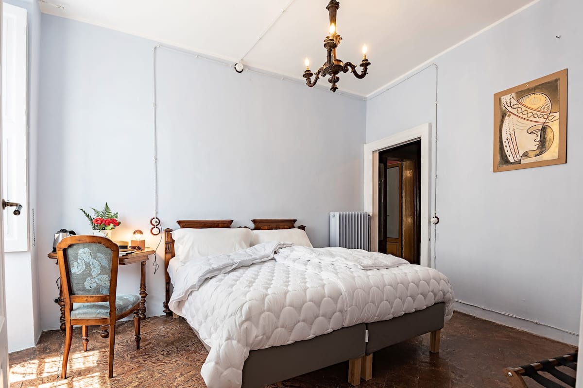 A bedroom with a bed, a chair, a desk, and a radiator.