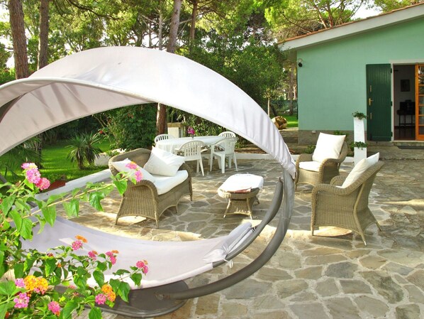 An outdoor patio with wicker furniture, a covered seating area, and a stone floor.