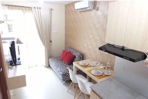 A compact living space with a sofa, a dining table set for two, and a small kitchenette area. - 1 BR Residence Woodland Park (Jakarta)