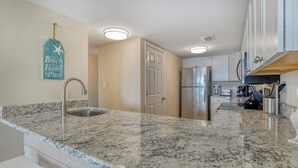 A modern kitchen with granite countertops, stainless steel appliances, and a hanging sign that reads "The Beach is my Happy Place." - Oceanfront Oasis - 2 Bedroom, 2 Bath Beautifully Renovated Oceanfront Condo (Garden City Beach)