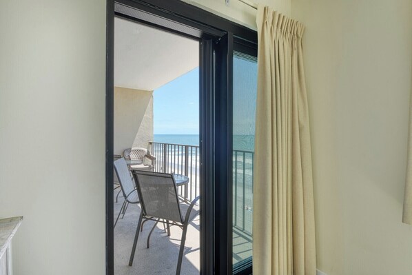 A balcony with a table and chairs, overlooking a beach.