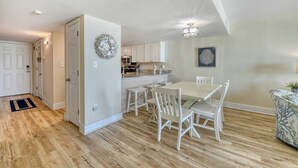 A modern kitchen with white cabinets, a dining table with white chairs, and a decorative wreath on the wall. - Oceanfront Oasis - 2 Bedroom, 2 Bath Beautifully Renovated Oceanfront Condo (Garden City Beach)