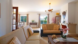 Un salon comprenant un canapé, une table basse et une cheminée. On aperçoit également un coin repas avec une table et des chaises à travers une porte vitrée.